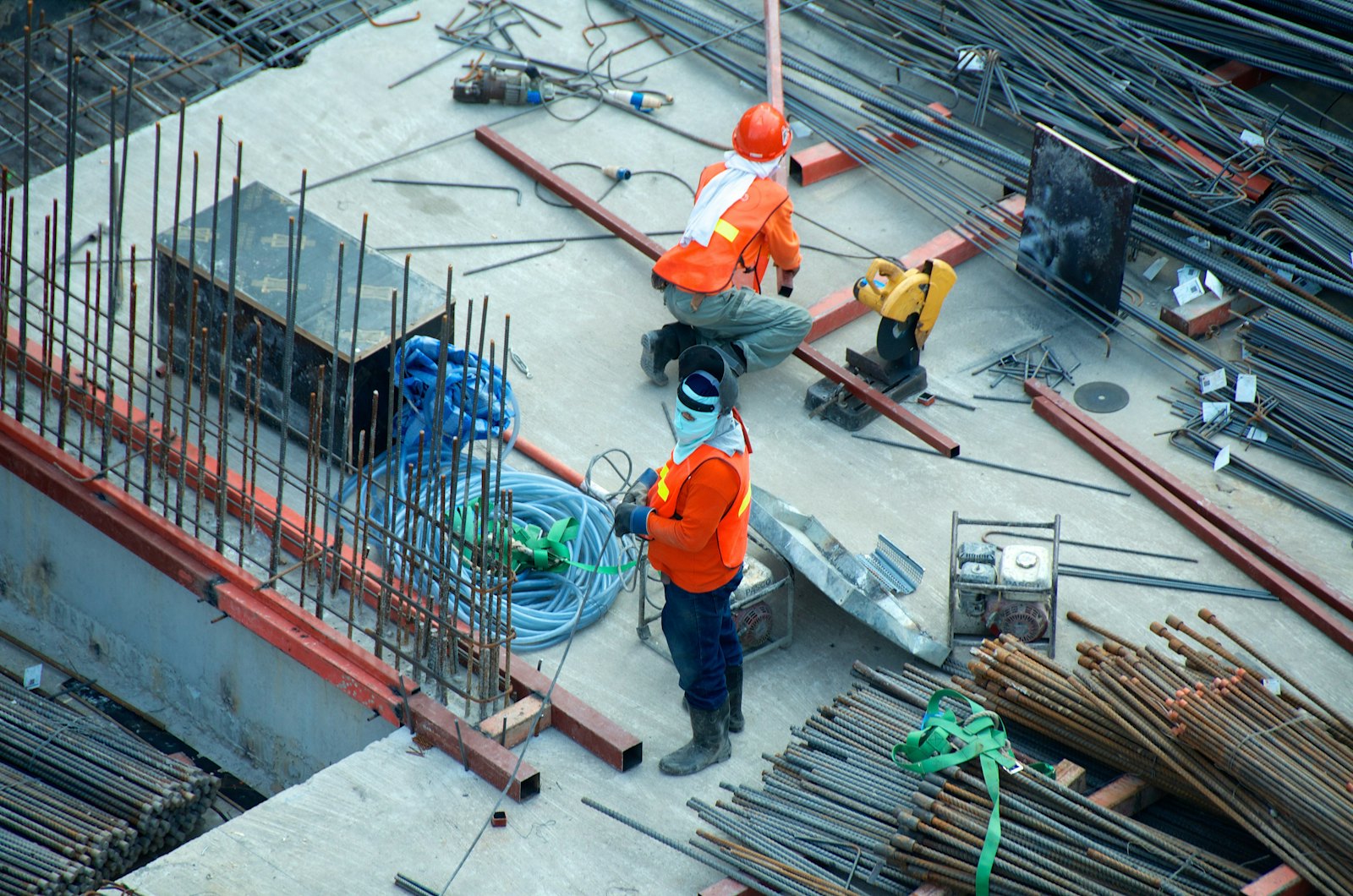 Two construction workers in hard hats and high-visibility vests fixing reinforcement steel on a concrete deck